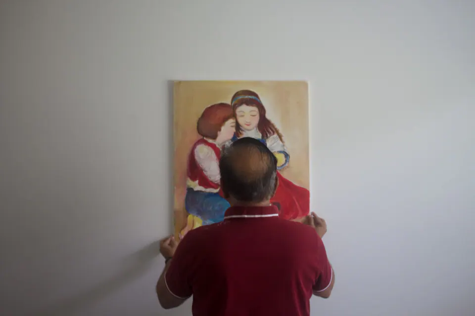 Person in a red shirt seen from behind while hanging a painting of two seated children.