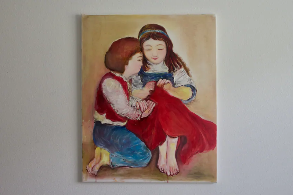 Two seated children in red and blue clothing, one whispering while the other sews red fabric.